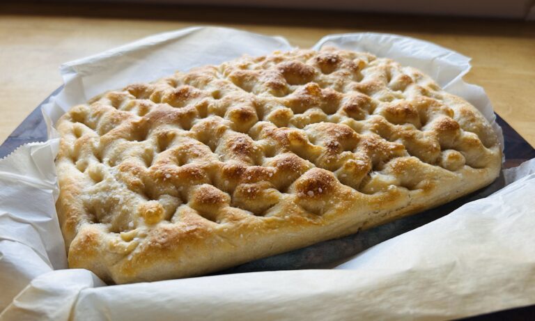 Freshly bakes sourdough focaccia bread sitting on parchment paper.