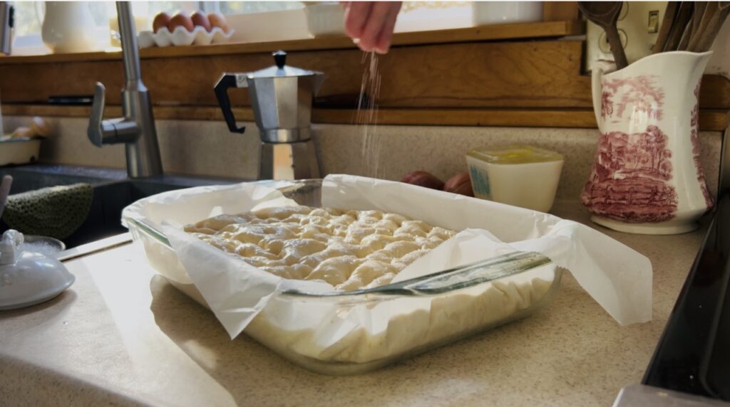 Sprinkling focaccia dough with flaky salt. 