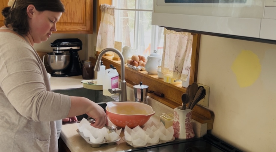 Woman scooping cupcake batter into lined cupcake tins.