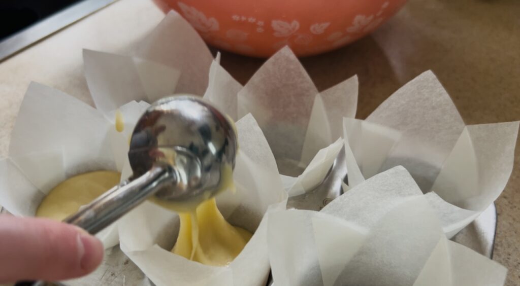 Scooping cupcake batter into cupcake cups for baking.