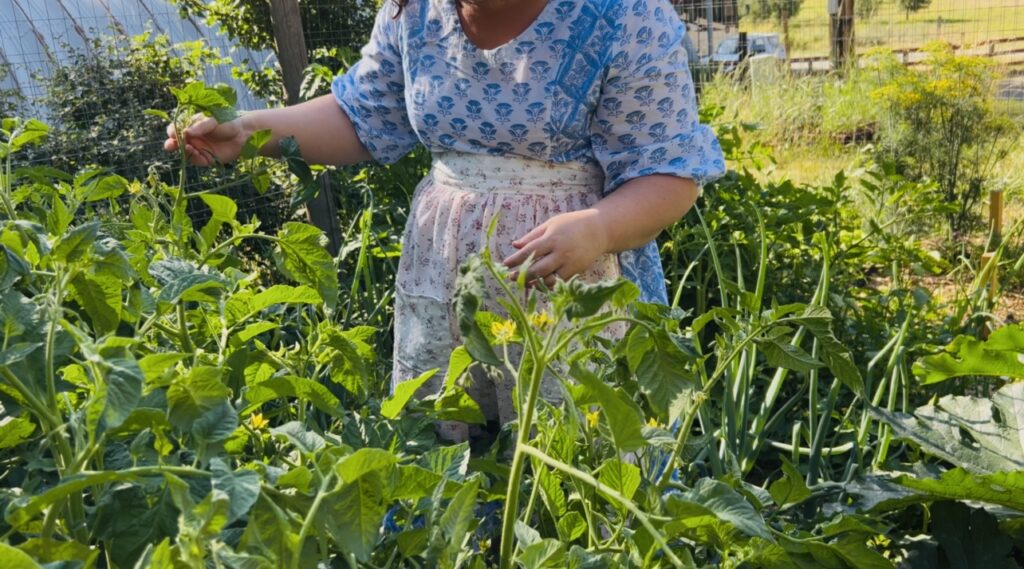Woman standing in a garden wearing a blue and white dress with a cottage waist apron.