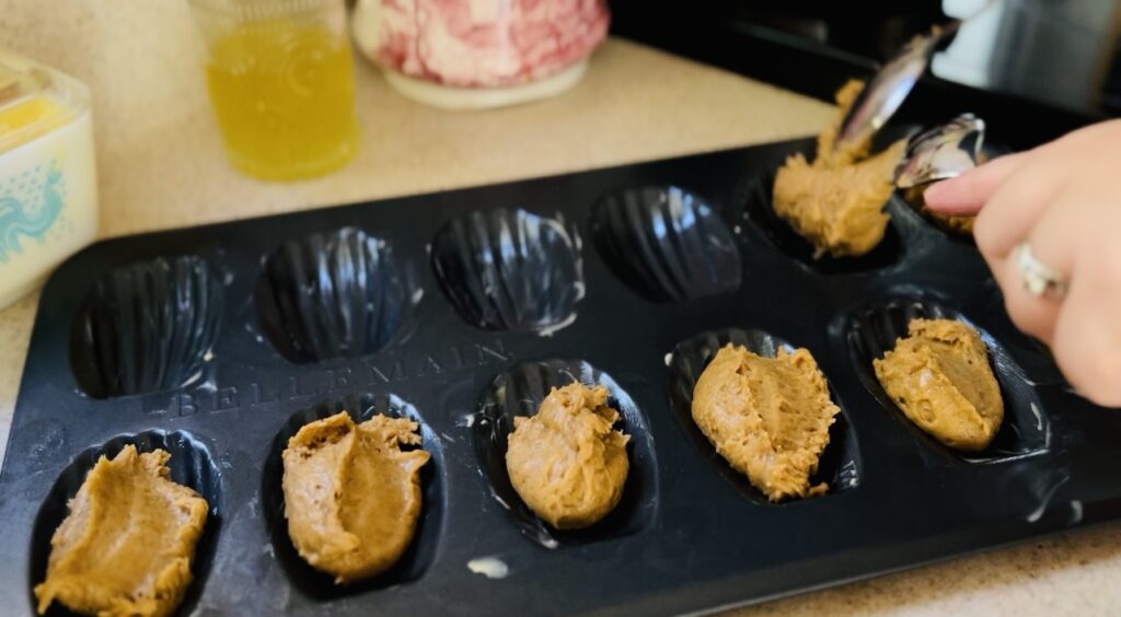 Scooping Madeleine cookie dough into a Madeleine cookie mold for baking.